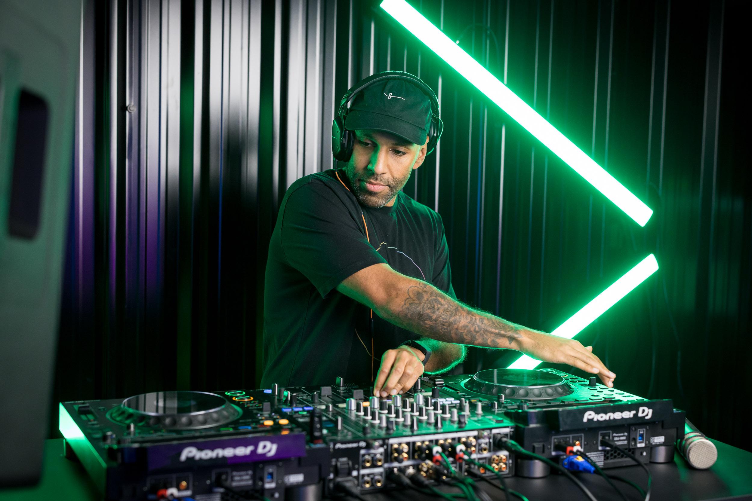 Crossfader DJ tutor mixing on Pioneer decks under green neon studio lighting.
